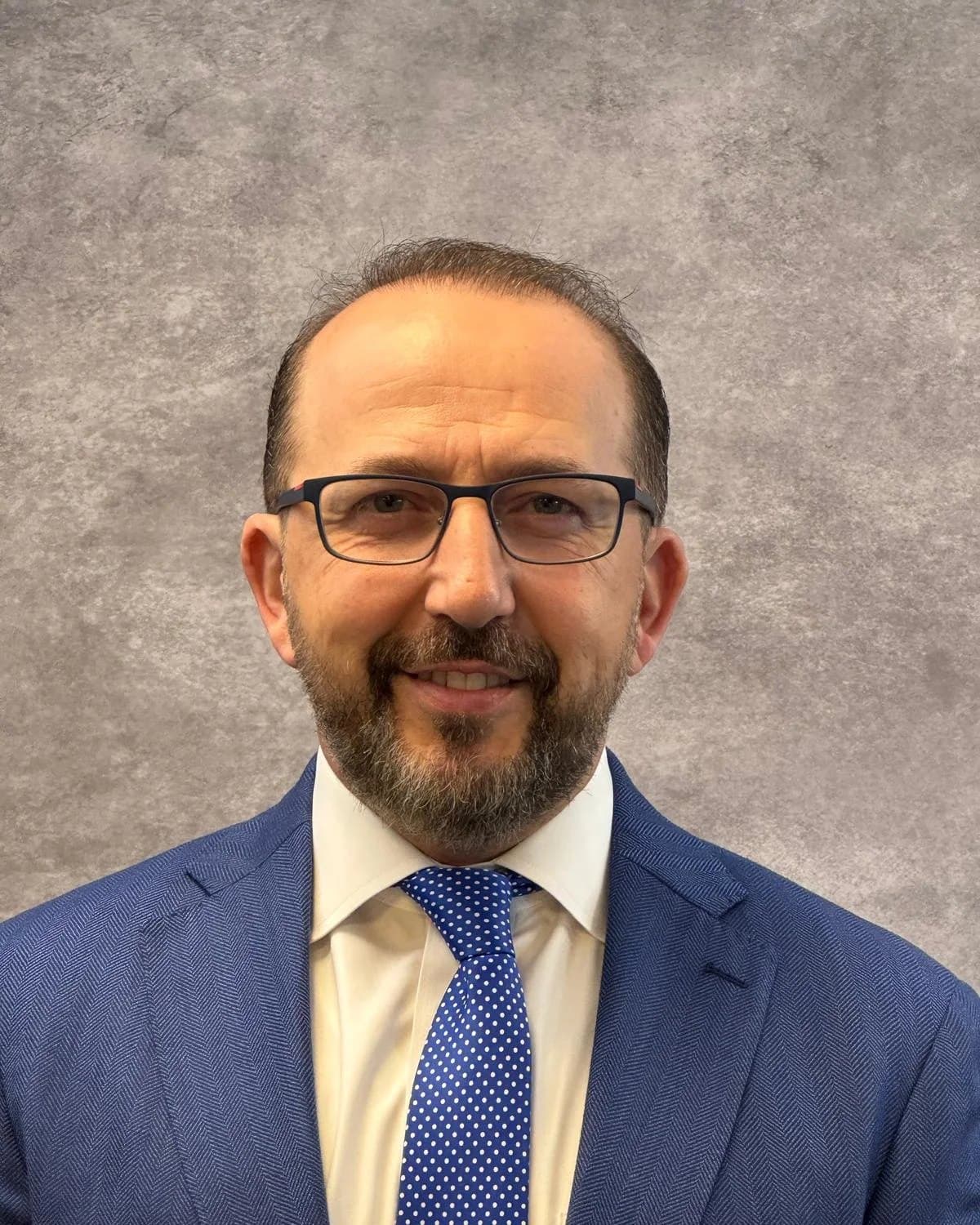 Dr. Ihab Herraka, MD, in a navy suit and glasses against a grey backdrop